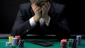 Person in a suit sitting at a poker table with their head in their hands appearing frustrated.