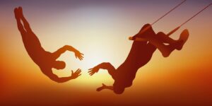 The image depicts two trapeze artists mid-air against a sunset background, with one reaching out to catch the other in an act of trust and synchronization.