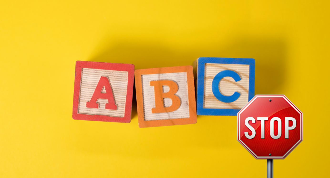 The image features three wooden alphabet blocks labeled "A," "B," and "C" against a bright yellow background, with a red stop sign placed beside them.