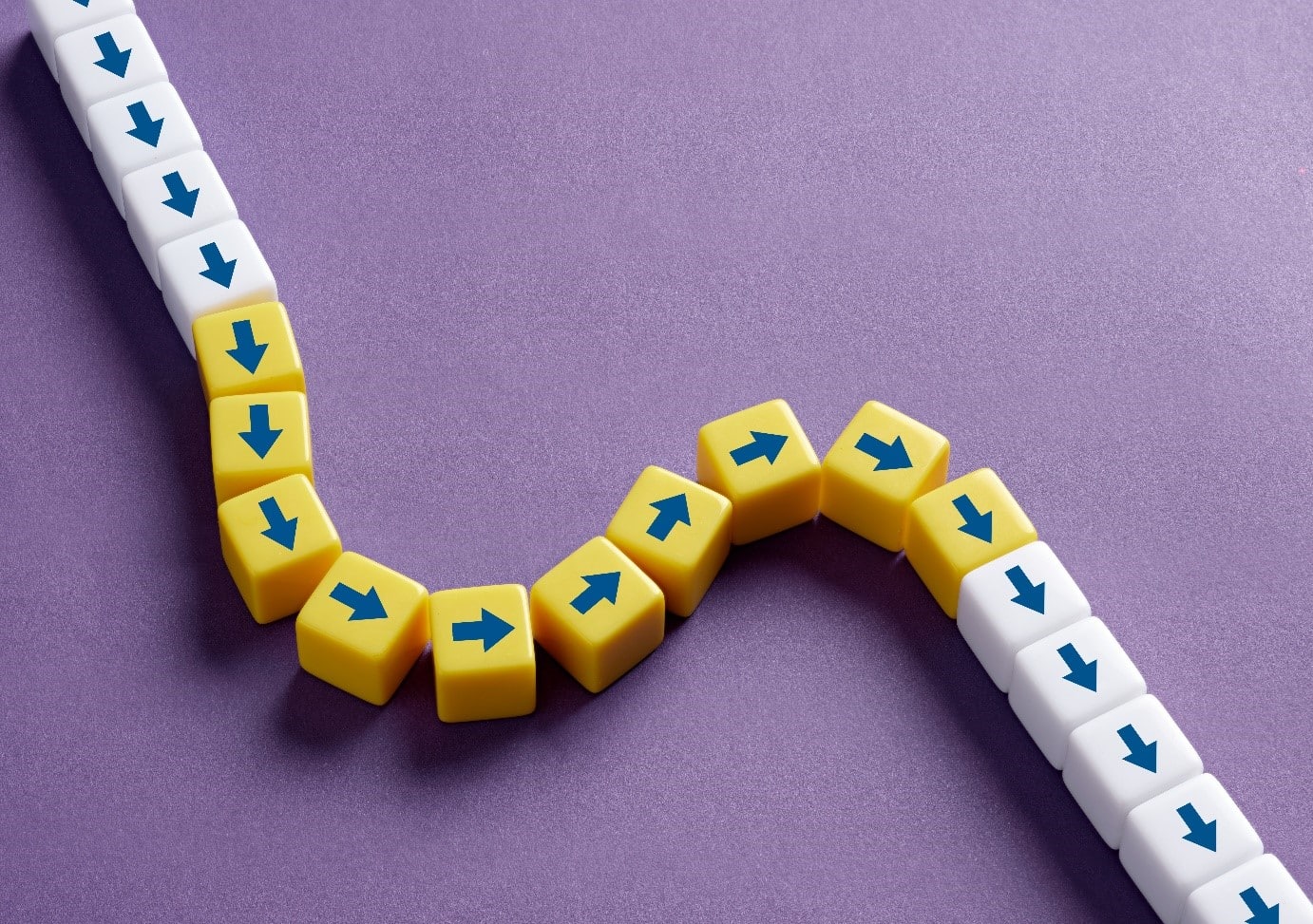 A chain of small white and yellow cubes with blue arrows is arranged on a purple background. The white cubes form a straight path, while the yellow cubes introduce a curved deviation, symbolizing a disruption or change in direction.