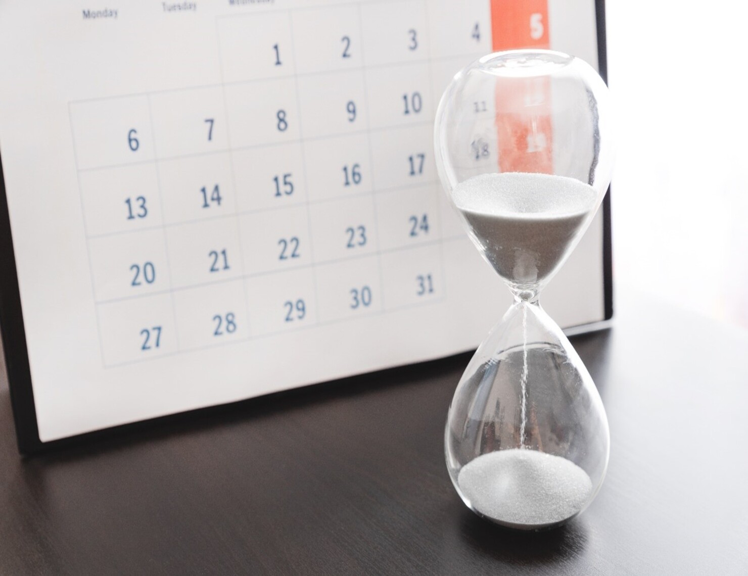 hourglass in front of calendar page, representing end-of-the-month demand signal distortion