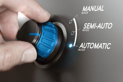 Una mano gira un dial con tres configuraciones: modo manual, modo semiautomático y modo automático. El dial está actualmente configurado en Modo Automático, como lo indica una luz azul encendida al lado de la etiqueta. El fondo está difuminado, destacando la esfera y la aguja.