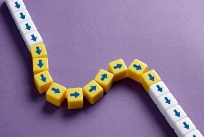 A chain of small white and yellow cubes with blue arrows is arranged on a purple background. The white cubes form a straight path, while the yellow cubes introduce a curved deviation, symbolizing a disruption or change in direction.