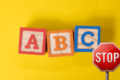 The image features three wooden alphabet blocks labeled "A," "B," and "C" against a bright yellow background, with a red stop sign placed beside them.