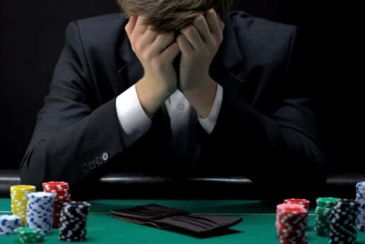 Person in a suit sitting at a poker table with their head in their hands appearing frustrated.