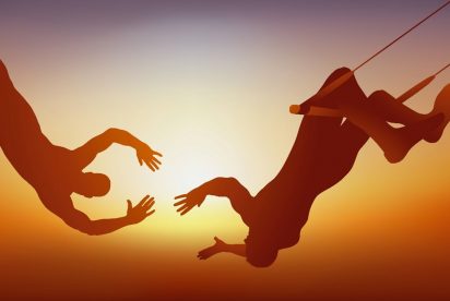 The image depicts two trapeze artists mid-air against a sunset background, with one reaching out to catch the other in an act of trust and synchronization.